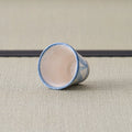 Sandy stoneware cup with a blue pattern, tipped on its side showing the interior.