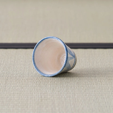 Sandy stoneware cup with a blue pattern, tipped on its side showing the interior.