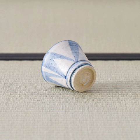 Sandy stoneware cup with a blue geometric pattern, tipped over to show its foot, on a tatami mat.