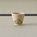 Sandy stoneware cup with a green-and-blue dotted band, upright front view on a tatami mat.