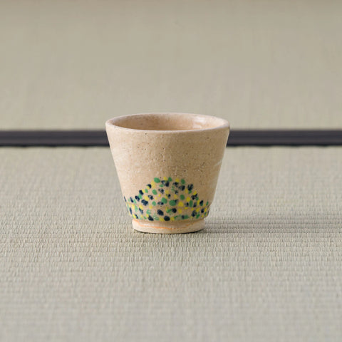 Sandy stoneware cup with a green-and-blue dotted band, upright front view on a tatami mat.