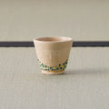 Sandy stoneware cup with a green-and-blue dotted band, side view on a tatami mat.