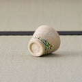 Sandy stoneware cup with a dotted band, tipped over to show its foot, on a tatami mat.