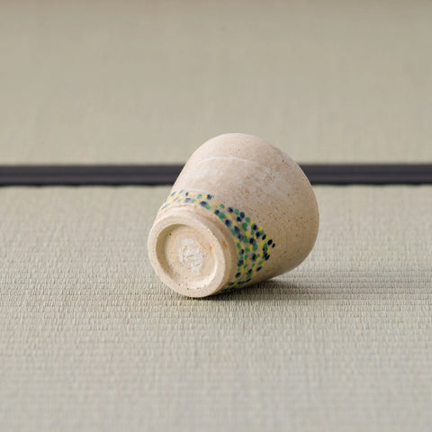 Sandy stoneware cup with a dotted band, tipped over to show its foot, on a tatami mat.