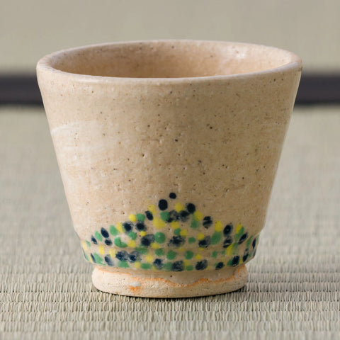 Close view of a sandy stoneware cup with a green-and-blue dotted band.