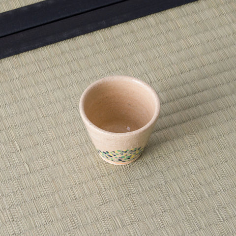 Sandy stoneware cup with a green-and-blue dotted band, front view on a tatami mat.
