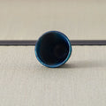 Deep blue speckled cup tipped over to show its dark interior, on a tatami mat.