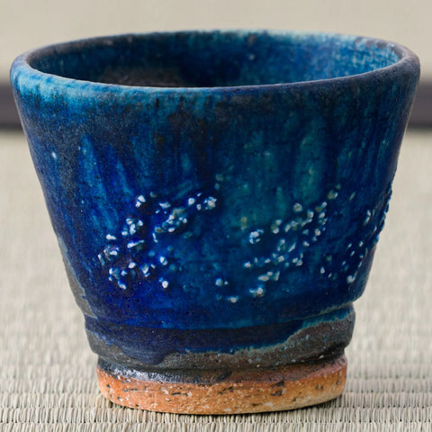 Deep blue speckled glazed cup with an unglazed foot, close view on a tatami mat.