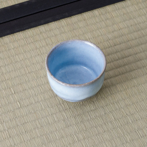 Small pale blue glazed cup, three-quarter view showing the interior, on a tatami mat.