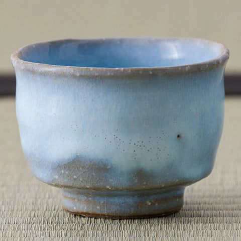 Pale blue crackle-glazed teacup, close side view on a tatami mat.