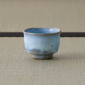 Pale blue crackle-glazed ceramic teacup viewed from the side on a tatami mat.