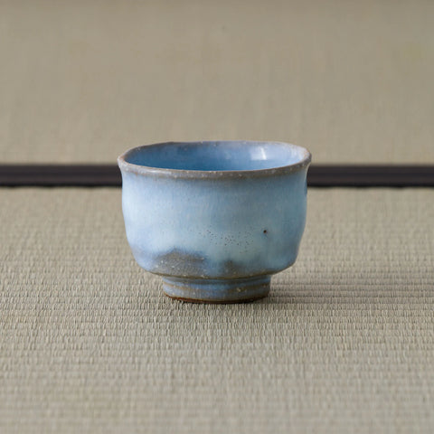 Pale blue crackle-glazed ceramic teacup viewed from the side on a tatami mat.