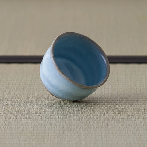 Pale blue crackle-glazed ceramic teacup tipped on its side to show the glazed interior, on a tatami mat.