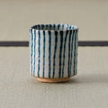 White cup with blue vertical stripes, front view on a tatami mat.