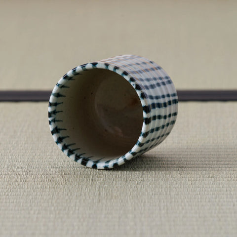 White cup with blue vertical stripes tipped over to show its interior, on a tatami mat.