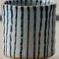 White cup with blue-green vertical stripes, close view on a tatami mat.