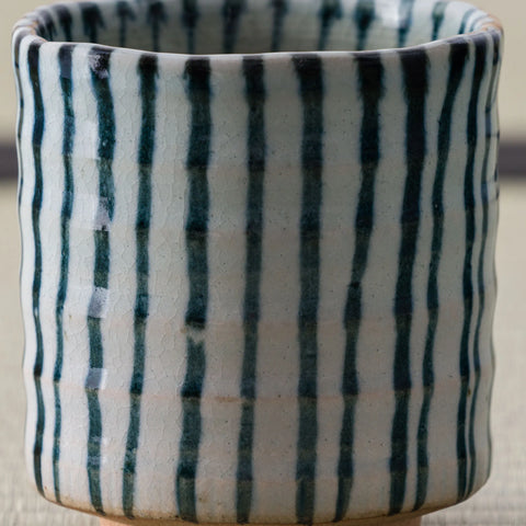 White cup with blue-green vertical stripes, close view on a tatami mat.