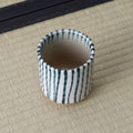 White cup with blue vertical stripes, viewed from above showing the interior, on a tatami mat.
