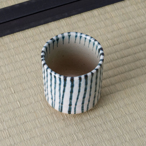 White cup with blue vertical stripes, viewed from above showing the interior, on a tatami mat.