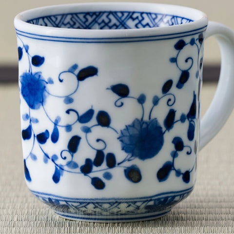 White porcelain mug with a blue floral scroll design and handle, front view on a tatami mat.