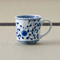 White porcelain mug with a blue floral scroll design and handle, side view on a tatami mat.