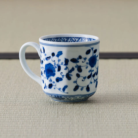 White porcelain mug with a blue floral scroll design and handle, front view on a tatami mat.