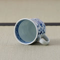 White porcelain mug with a blue floral design tipped over to show its interior and handle.