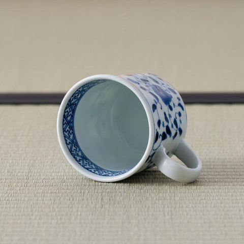 White porcelain mug with a blue floral design tipped over to show its interior and handle.