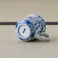 White porcelain mug with a blue floral design tipped over to show its marked base.