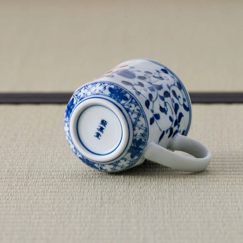 White porcelain mug with a blue floral design tipped over to show its marked base.