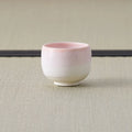 Cup glazed pink fading to white, side view on a tatami mat.
