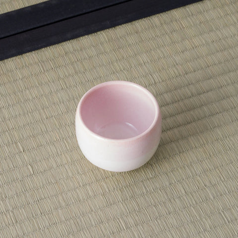 Pale pink glazed cup viewed from above, showing the interior, on a tatami mat.