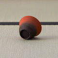 Red-to-dark gradient cup tipped over to show its dark foot, on a tatami mat.
