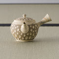 Beige polka-dot kyusu teapot, three-quarter view with the spout to the left