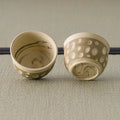 The two matching beige cups, one tipped to show the brushwork inside