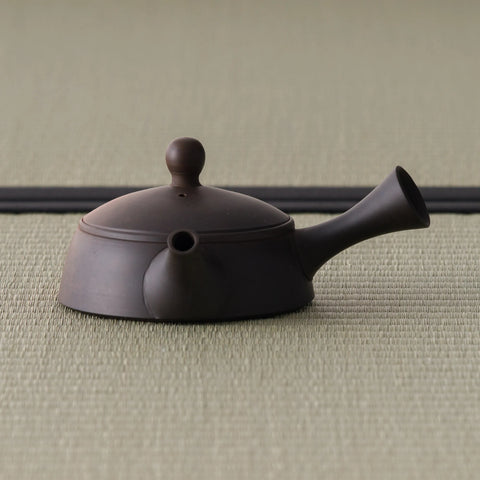 Two-tone unglazed kyusu teapot, three-quarter view showing the dark upper body and reddish lower body