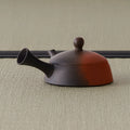 Two-tone clay kyusu with the back of the handle to the left, showing the reddish-and-dark fired surface