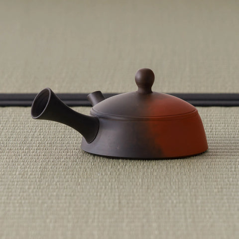 Two-tone clay kyusu with the back of the handle to the left, showing the reddish-and-dark fired surface
