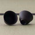 The two matching black teacups, one upright and one tilted to show the smooth interior