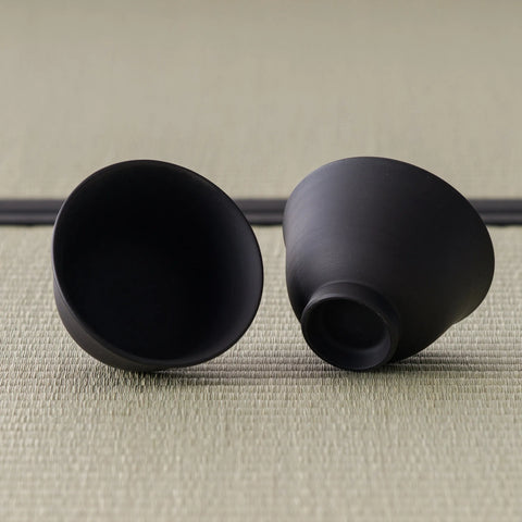 The two matching black teacups, one upright and one tilted to show the smooth interior