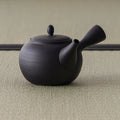 Black kyusu teapot showing the rounded body and side handle from the rear three-quarter