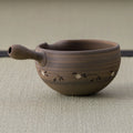 Brown stoneware spouted bowl (katakuchi) with an inlaid floral band, side view showing the spout.