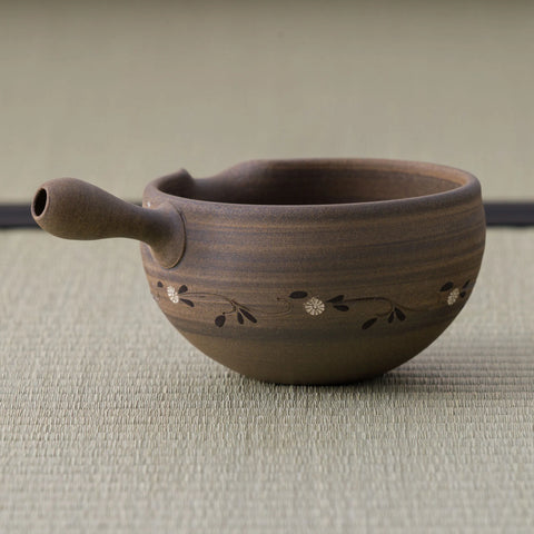 Brown stoneware spouted bowl (katakuchi) with an inlaid floral band, side view showing the spout.