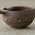 Brown stoneware spouted bowl (katakuchi) with an inlaid floral band, close side view.