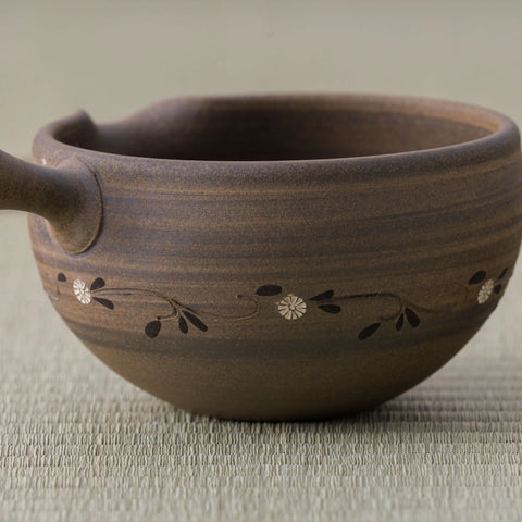 Brown stoneware spouted bowl (katakuchi) with an inlaid floral band, close side view.