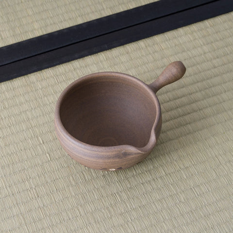 Brown stoneware spouted bowl (katakuchi) viewed from above showing its interior, on a tatami mat.