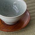 The reddish-brown wooden chataku shown in use with a pale celadon teacup resting on it