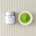Silver Tezumi tin of Uji-no-Mori (宇治の杜) matcha beside a small dish of green matcha powder on a tatami mat.