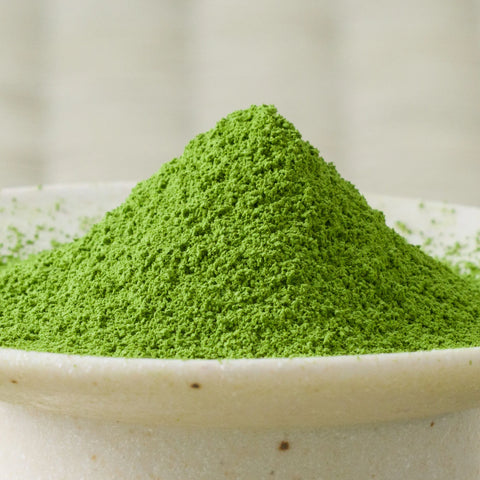 Bright green Uji-no-Mori matcha powder mounded in a ceramic bowl, side view.