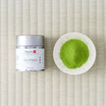 Silver Tezumi tin of Uji-Hikari (宇治光) matcha beside a small dish of green matcha powder on a tatami mat.